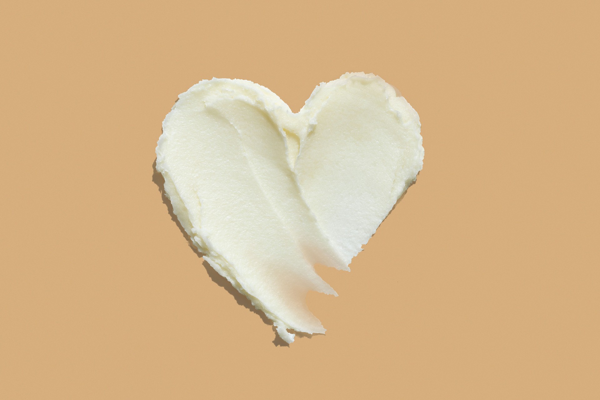 Heart shape from thick shea butter cream moisturiser on brown beige background. Skin care product texture heart