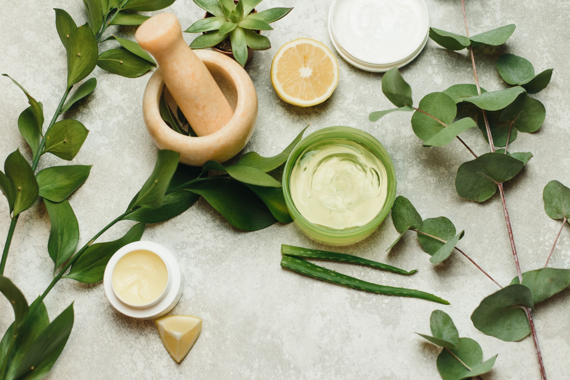 Flat lay composition with cosmetic products on grey background. Cans of natural cream and gel, mortar for mixing ingredients. Natural skin care beauty products